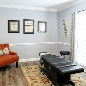 Modern chiropractic treatment room featuring an adjustment table and seating area.